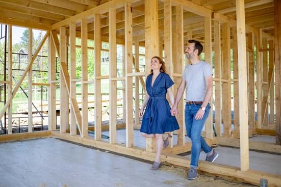 Young couple holding hands walking through the a new house being constructed.